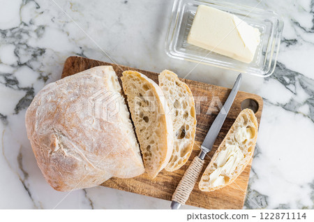 Sliced ciabatta bread with fresh butter on a wooden cutting board. marble background. top view Sliced ciabatta bread with fresh butter on a wooden cutting board. marble background. top view 122871114