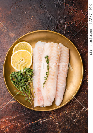 Raw cod loin pieces, whitefish fillets without skin on plate with herbs. brown background. top view Raw cod loin pieces, whitefish fillets without skin on plate with herbs. brown background. top view 122871148