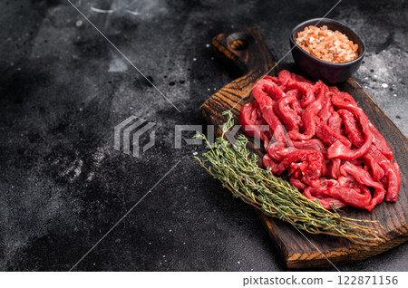 Uncooked Raw beef sliced meat, strips for cooking beef stroganoff on wooden board. black background. top view 122871156