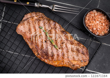 Grilled Striploin steak, New York strip beef meat steak on a rack. black background. top view Grilled Striploin steak, New York strip beef meat steak on a rack. black background. top view 122871164