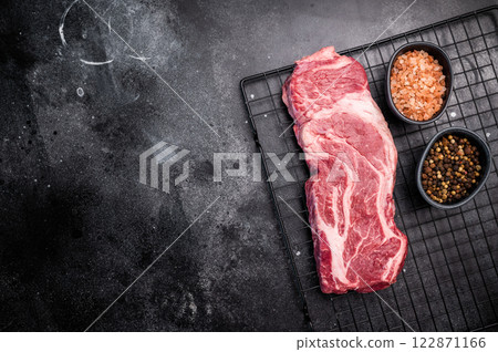 Ready for cooking Chuck eye roll steak, fresh raw beef meat on a rack. black background. top view 122871166