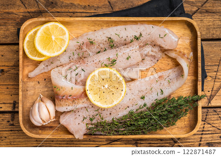 Raw Pollock and Hake fish fillets on a wooden board with herbs ready for cooking. wooden background. top view 122871487