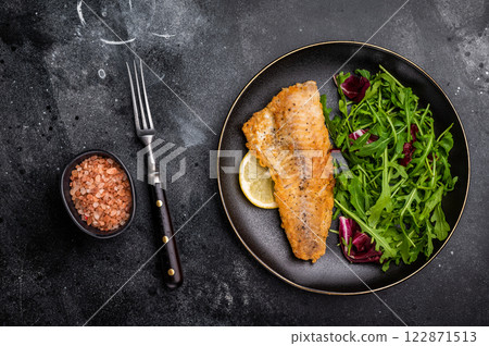 Roasted Haddock fish fillet on a plate with salad. black background. top view Roasted Haddock fish fillet on a plate with salad. black background. top view 122871513