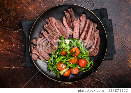 Grilled and sliced Beef Denver strip Steak on a plate with salad. brown background. top view Grilled and sliced Beef Denver strip Steak on a plate with salad. brown background. top view 122871522