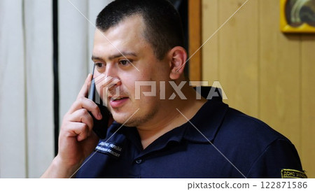 Male firefighter chief have serious telephone conversation with his subordinate by smartphone at fire station. Nervous fireman talking by mobile phone at fire department. Concept of heroic profession 122871586