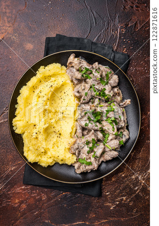 Beef stroganoff with mashed potatoes, fresh greenery and savory mushroom sauce in a plate . brown background. top view 122871616