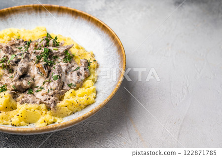 Plate of tender beef stroganoff served with creamy mashed potatoes and steaming gravy. grey background. top view Plate of tender beef stroganoff served with creamy mashed potatoes and steaming gravy. grey background. top view 122871785