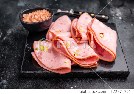Mortadella Bolognese sausage slices with pistachios. black background. top view Mortadella Bolognese sausage slices with pistachios. black background. top view 122871795