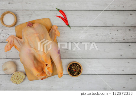 A raw processed chicken carcass lies on a white wooden background on a wooden board with spices and salt in wooden bowls, garlic and red pepper with space for text. The concept of cooking, wholesome A raw processed chicken carcass lies on a white wooden background on a wooden board with spices and salt in wooden bowls, garlic and red pepper with space for text. The concept of cooking, wholesome 122872333