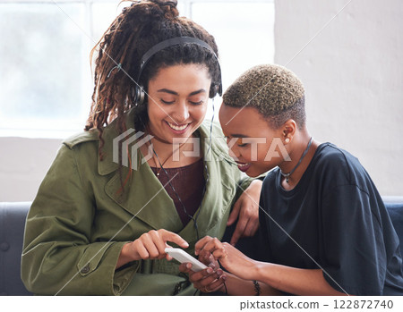 female friends using smartphone listening to music at home with woman wearing headphones female friends using smartphone listening to music at home with woman wearing headphones 122872740