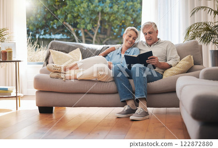 Retirement senior couple with photo album book on sofa together in summer house for vacation holiday. Happy elderly woman or people relax on couch in living room reading, talking of marriage history Retirement senior couple with photo album book on sofa together in summer house for vacation holiday. Happy elderly woman or people relax on couch in living room reading, talking of marriage history 122872880