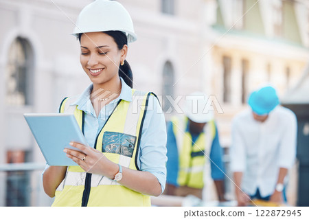 Construction, building and tablet with a woman architect working in the city on a build site with her team in the background. Engineer, designer and architecture with a young female at work online 122872945