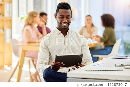 African businessman working on a digital tablet while sitting by his desk in a corporate office. Happy, professional and black man doing research on the internet or a website with a mobile device. 122873047