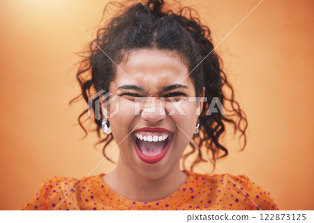 Happiness, smile and portrait of a fun woman model screaming with joy in a bright studio. Face of a happy hispanic girl with trendy, stylish and colorful clothes standing by an orange background. 122873125