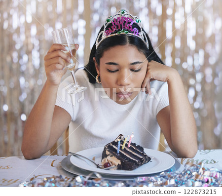 Sad woman birthday cake, celebrate home alone with champagne and sad at lonely pandemic party celebration. Young latino girl fail to blow candle on table, wish thinking and shiny crown decoration Sad woman birthday cake, celebrate home alone with champagne and sad at lonely pandemic party celebration. Young latino girl fail to blow candle on table, wish thinking and shiny crown decoration 122873215