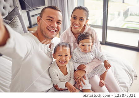Selfie, family and children with a mother, father and their girl kids sitting on a bed in their home. Daughter, sister and parents with a man taking a picture while relaxing in a bedroom of the house 122873321