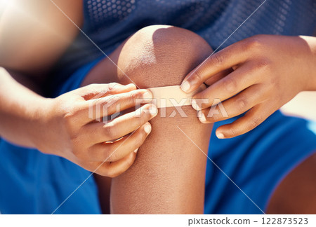 Children, accident and plaster with a band aid on the knee of boy with an injury, wound or pain. Kids, cut and heal with the hands of a male child outside with a scrape, bruise or injured anatomy 122873523
