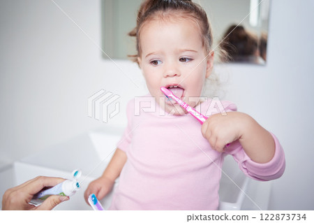 Baby learning to brush her teeth, dental and oral hygiene. Toothbrush, toothpaste and brushing teeth in child development and routine. Dentist, dentistry and teeth cleaning in young children. 122873734
