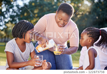 Black woman, park and children family drinks juice for healthy nutrition or wellness nutritionist diet on picnic. Mother with girl kids or black people smile with citrus fruit orange juice in summer 122873738