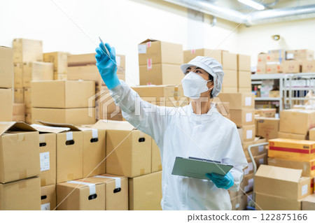A worker wearing a white coat and inspecting the warehouse 122875166