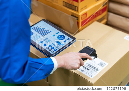 A worker manages package information using a handheld scanner and tablet. 122875196