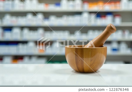 Wooden mortar and pestle on pharmacy counter with blurred drug shelves in pharmacy background 122876346