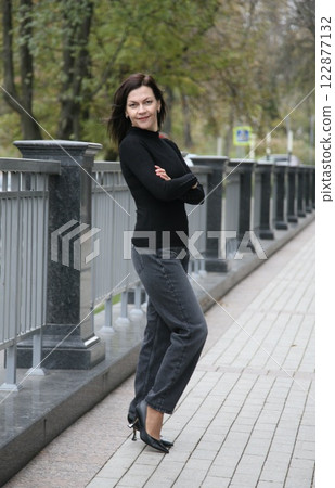 Pretty middle age brunette woman 51+ years old in modern graphite mom jeans poses with crossed arms and looks at the camera Pretty middle age brunette woman 51+ years old in modern graphite mom jeans poses with crossed arms and looks at the camera 122877132