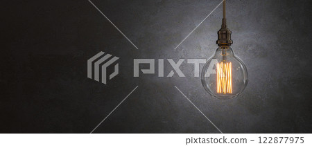 Glowing light bulb hanging on dark background providing illumination Glowing light bulb hanging on dark background providing illumination 122877975