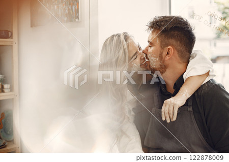 Mutual creative work. Young beautiful couple in casual clothes and aprons. People creating a bowl on a pottery wheel in a clay studio. Mutual creative work. Young beautiful couple in casual clothes and aprons. People creating a bowl on a pottery wheel in a clay studio. 122878009