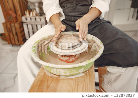 Female potter working with clay on wheel in studio. Clay with water splattered around the potter wheel. 122878027
