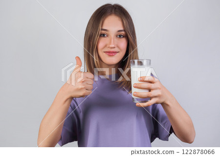 Portrait of a satisfied young woman in a purple t-shirt drinking milk from the glass isolated over light background Portrait of a satisfied young woman in a purple t-shirt drinking milk from the glass isolated over light background 122878066