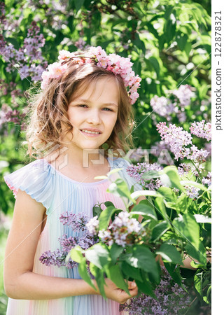 young girl with curly blonde hair standing among blooming lilac bushes in sunlit garden. soft lighting and natural setting create dreamy atmosphere, evoking themes of innocence, childhood, 122878321