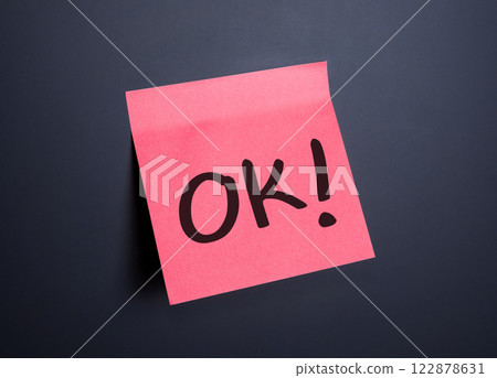 A bright pink sticky note displays the word OK on a dark background A bright pink sticky note displays the word OK on a dark background 122878631