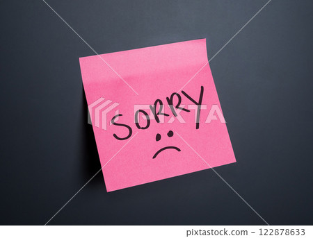 A pink sticky note displays the word sorry alongside a sad face emoticon A pink sticky note displays the word sorry alongside a sad face emoticon 122878633