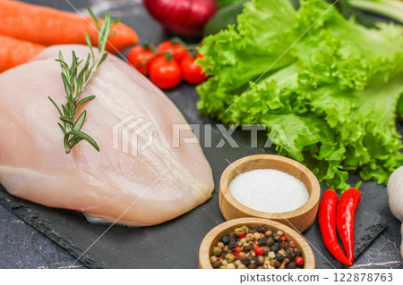 Chicken diet breast with a sprig of rosemary on top lying surrounded by herbs, seasonings and vegetables on a dark background close-up. The concept of healthy eating, dietary and natural products Chicken diet breast with a sprig of rosemary on top lying surrounded by herbs, seasonings and vegetables on a dark background close-up. The concept of healthy eating, dietary and natural products 122878763