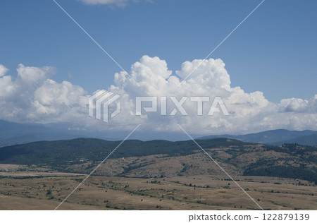 Panoramic photo of white air clouds floating low over a mountain range in sunny weather. Panoramic photo of white air clouds floating low over a mountain range in sunny weather. 122879139