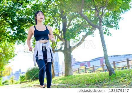 A cool woman jogging on a road with sunlight filtering through the trees Walking Diet Exercise Morning Color Diagonal 122879147