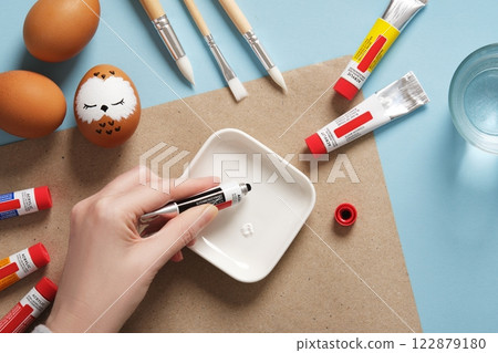 Women's hands squeeze black paint from a tube onto a palette. Preparation for the celebration of Easter. Coloring Easter eggs with acrylic pigment paints 122879180