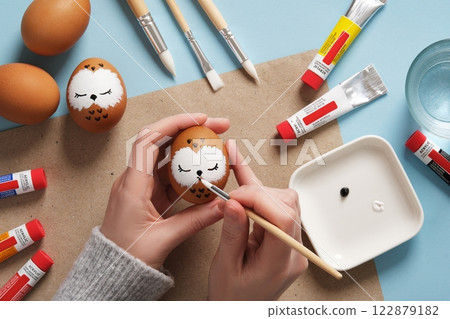 Drawing a sleeping owl on an eggshell. Step 2: Draw the beak. Preparation for Easter celebration. Acrylic paints in tubes, water, brushes. 122879182