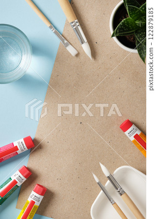 Preparing to draw. Tubes of acrylic paint, brushes, a glass of water on blue background. Place for your text. Preparing to draw. Tubes of acrylic paint, brushes, a glass of water on blue background. Place for your text. 122879185