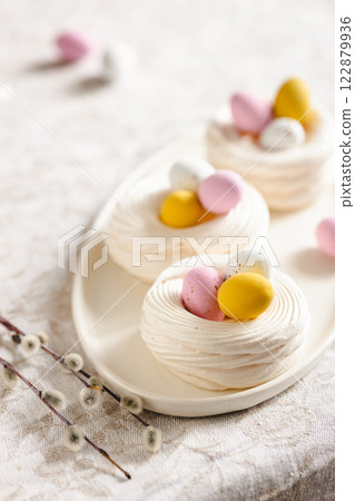 Easter meringue nests with colorful sweet eggs on plate, decorated willow twigs. Easter dessert closeup. 122879936
