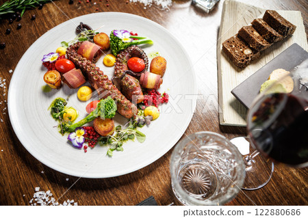 Grilled octopus tentacles with cherry tomatoes, broccoli, and edible flowers. Served with roasted potatoes, yellow sauce, and microgreens. Gourmet seafood dish in a modern restaurant 122880686