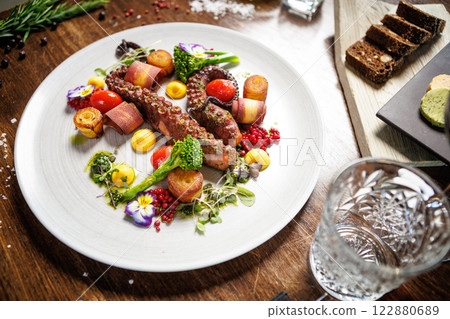 Octopus tentacles with cherry tomatoes, broccoli, and edible flowers. Accompanied by roasted potatoes, yellow sauce, and microgreens. Sophisticated seafood dish in a gourmet restaurant 122880689