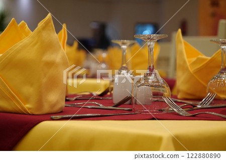 In a restaurant, yellow tablecloths, forks, knives lies on tables 122880890
