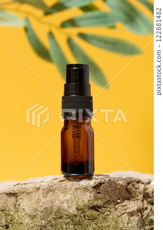 Brown glass bottle with dispenser stands on stone, yellow background 122881482