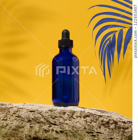 Blue glass bottle with black pipette and palm branch on yellow background, oil and cosmetics Blue glass bottle with black pipette and palm branch on yellow background, oil and cosmetics 122881607