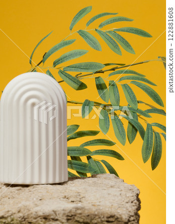 White ceramic arch on stone and branch with green leaves on yellow background, place for advertising and product display White ceramic arch on stone and branch with green leaves on yellow background, place for advertising and product display 122881608