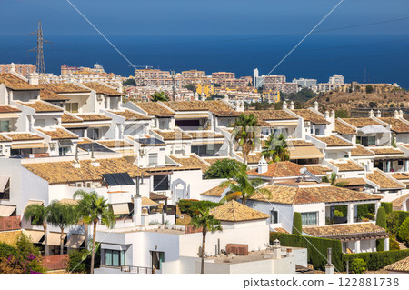Mediterranean coastal townhouses with terracotta roofs and palm trees, overlooking the sea. 122881738