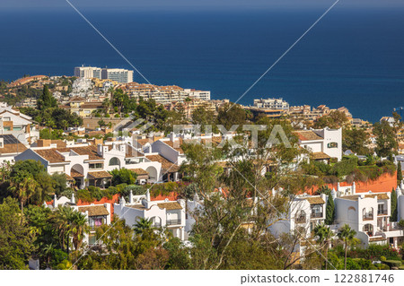 Coastal community homes overlooking the ocean. Whitewashed buildings and lush greenery against a deep blue sea. Coastal community homes overlooking the ocean. Whitewashed buildings and lush greenery against a deep blue sea. 122881746