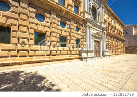 Exterior of the Palace of Charles V. Alhambra complex in Granada town, Andalusia, Spain. Grand palace entrance with intricate stonework and a large wooden door. 122881759
